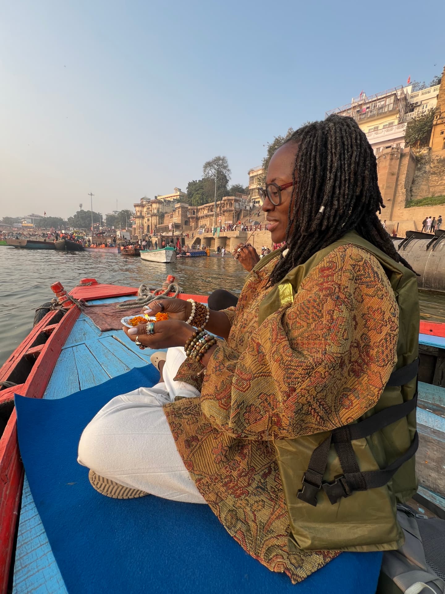 Dr. Makeba seated on a wooden boat on the Ganges holding marigold offerings
